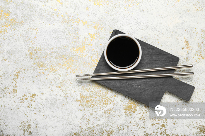 Bowl of soy sauce, chopsticks and cutting board on grunge background