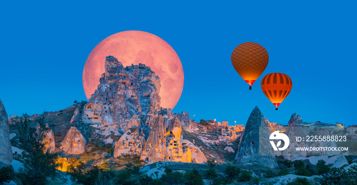 Hot air balloon flying over Uchisar castle with full moon  Elements of this image furnished by NASA