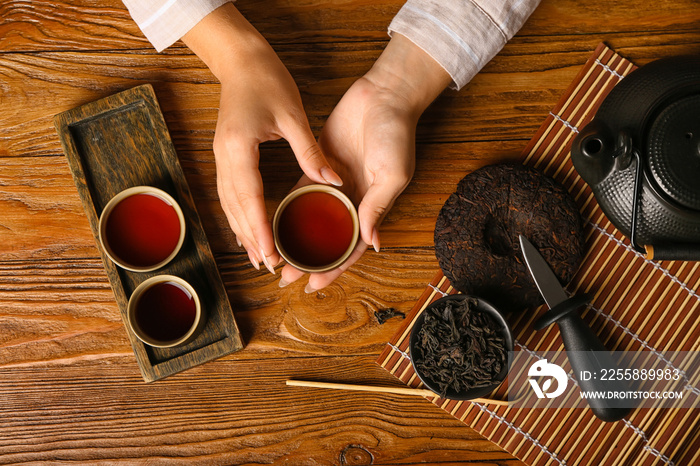 Female hands with cup of aromatic puer tea on wooden background