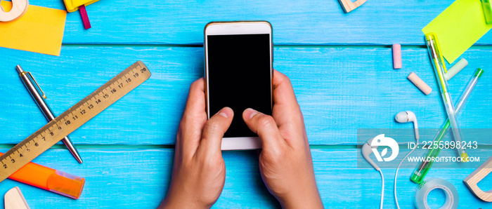 the student is holding a smartphone on the school board, digital diary or e-book,reluctance to learn, school supplies on a blue background. educational application. telephone addiction. top view.