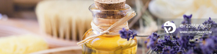 Concept of natural organic ingredients in cosmetology and home beauty treatment. Bottle of essential oil, lavender flowers, bath accessoires, wooden body brush. Close up, banner format