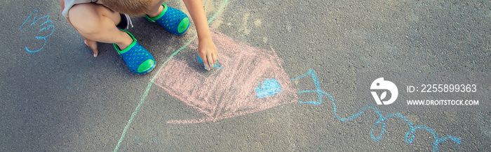 child draws a house in chalk on the pavement. Selective focus.