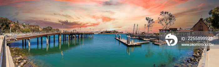 a stunning panoramic shot of a a harbor with blue ocean water and brown wooden piers and docked boats with red sky and powerful clouds at sunset at Baby Beach in Dana Point California USA