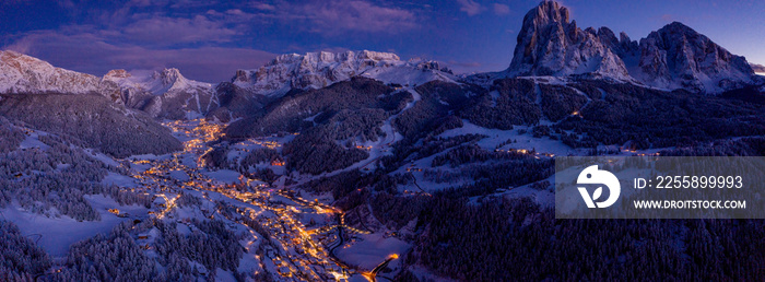 Beautiful panoramic view of Dolomites mountains at dusk during winter time. Magical winter mountain purple sunset with a mountain ski resort village. Christmas time.