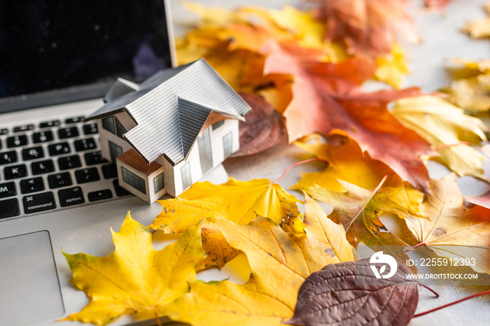 mockup model house and leaves near laptop computer on a table. Autumn season time