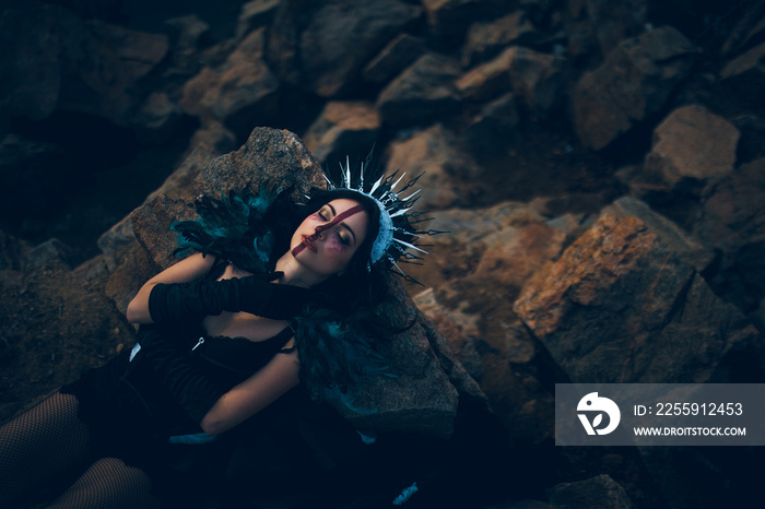 A young woman in the image of a fairy and a sorceress lying on rock.