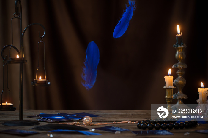 blue falling bird feathers over  wooden table with fortunetelling cards and antique candlesticks