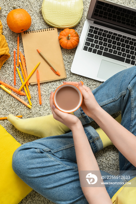 Woman with laptop drinking tasty pumpkin coffee on floor in room