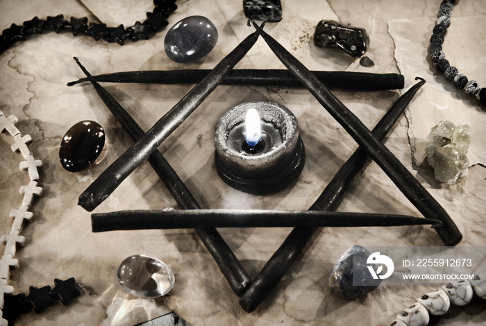Pentagram symbol made of black candles with crystal stones on paper.