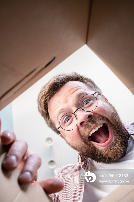 Happy man unpacks the delivered box with the parcel. Unpacking inside view.