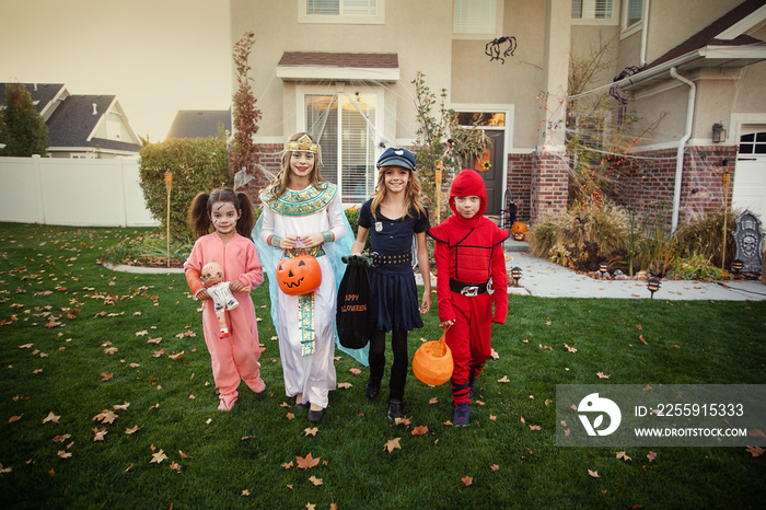 Group of kids dressed in Halloween costumes going trick or treating outdoors in October in a decorat