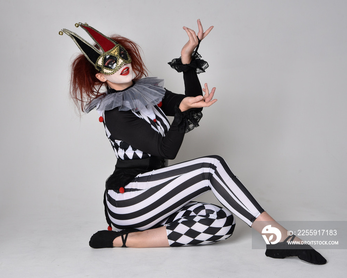 Full length  portrait of red haired  girl wearing a black and white clown jester costume, theatrical