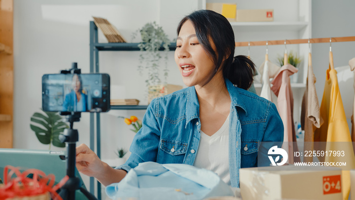 Young Asia lady fashion designer using mobile phone receiving purchase order and showing clothes rec