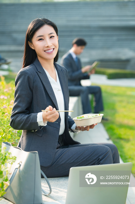 商务女性坐着户外边吃饭边工作