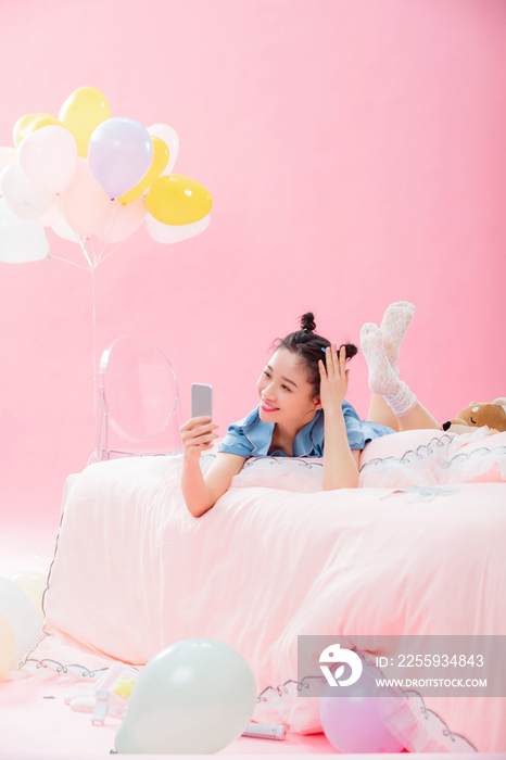 年轻女孩趴着在床上使用手机