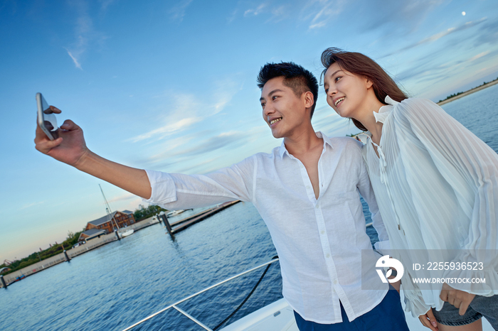 青年夫妇站在游艇上用手机拍照
