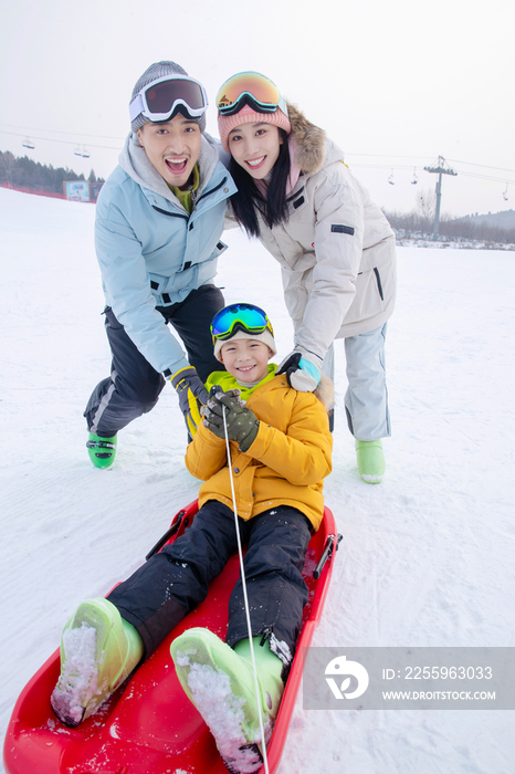 滑雪场上父母推着坐在雪上滑板的儿子