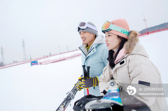 雪场上拿着滑雪板滑雪杖的快乐情侣