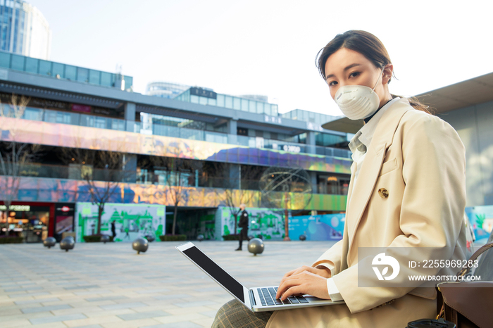 戴口罩的青年女人在户外使用电脑