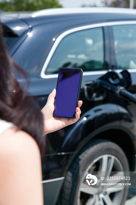 青年女人使用手机自助充电汽车