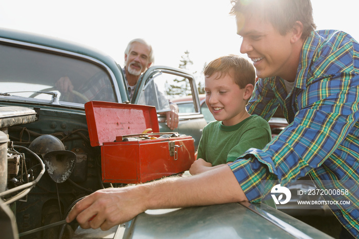 Three generations of males working on classic car.