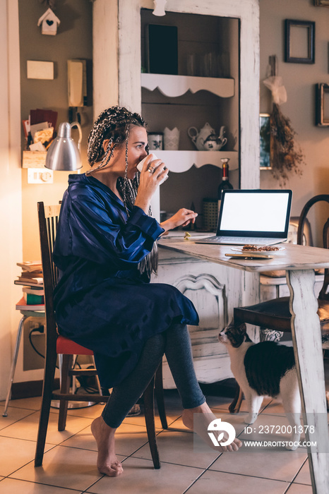 女性早上在家喝咖啡时使用笔记本电脑的侧视图
