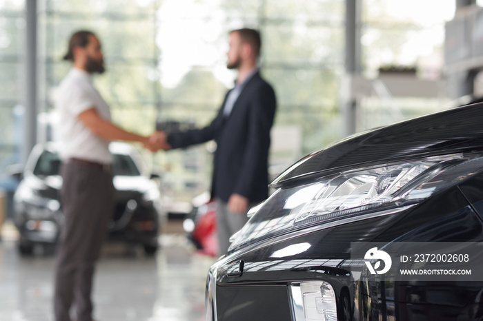 Men shaking hands in modern auto showroom.