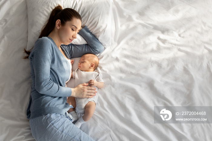 Co-sleeping with baby. Young woman napping in bed with her newborn child