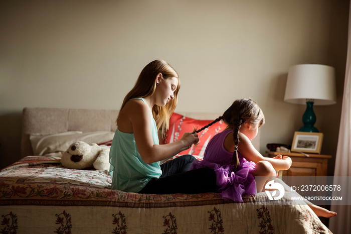 Girl braiding sisters hair on bed