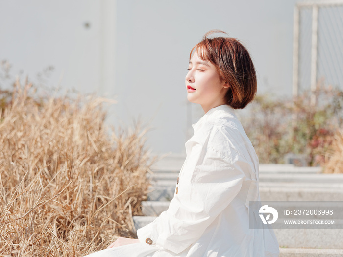 Beautiful young brunette woman in white shirt sit with eyes closed in sunny day. Outdoor fashion por