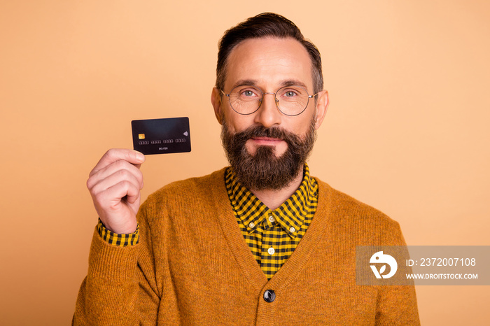 Portrait of mature man hold demonstrate credit card wear spectacles isolated over beige color backgr