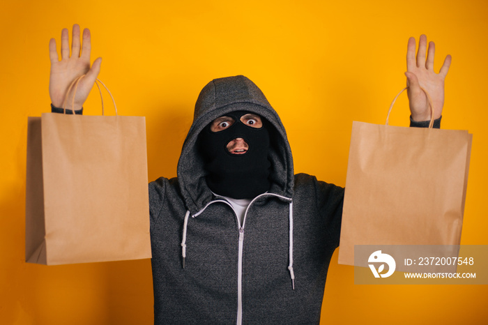 The thief with paper bags raised his hands to the top. The guy in the balaclava steals purchases fro