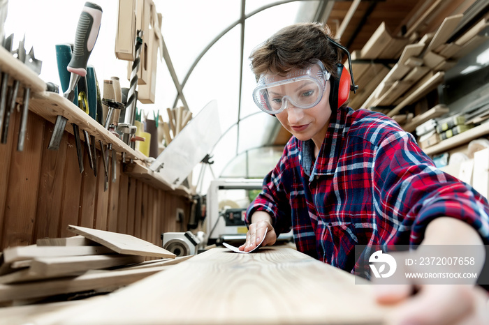 Young attractive 30-40 professional female carpenter looking grinding raw wood with sandpaper in car