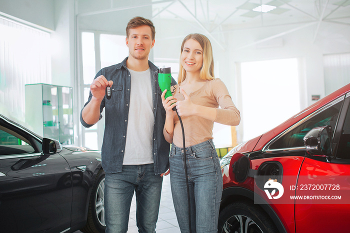 Young smiling family buying first electric car in the showroom. Environmental protection. Attractive