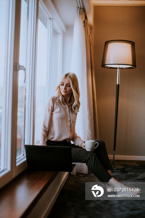 Young woman working on laptop  in living room on the window sill