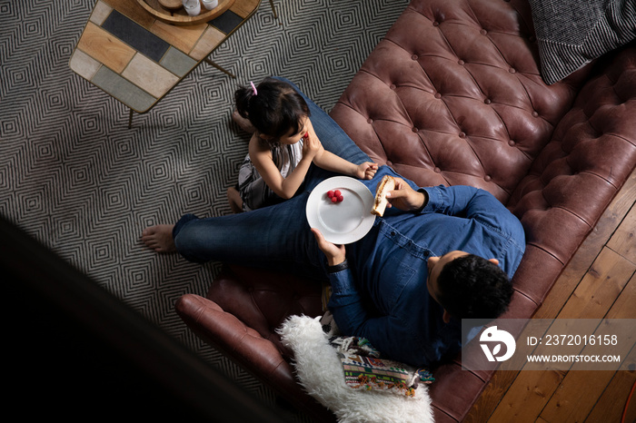 High angle view of father and daughter eating food on sofa