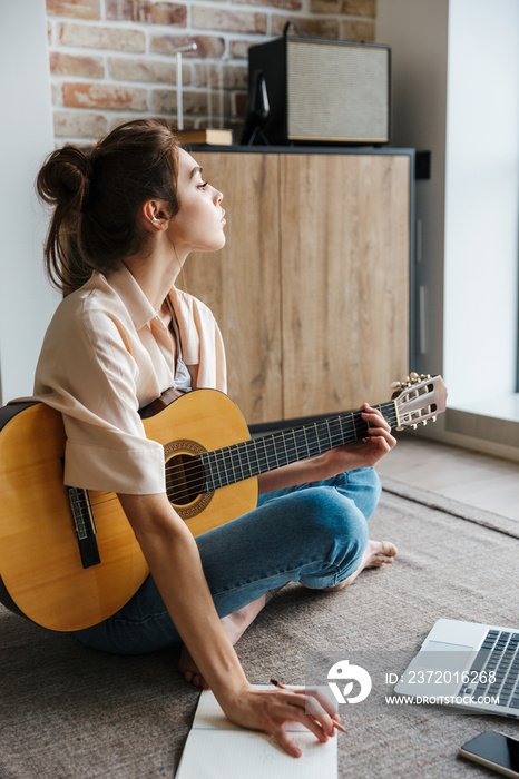 Image of young caucasian brunette woman playing acoustic guitar at home