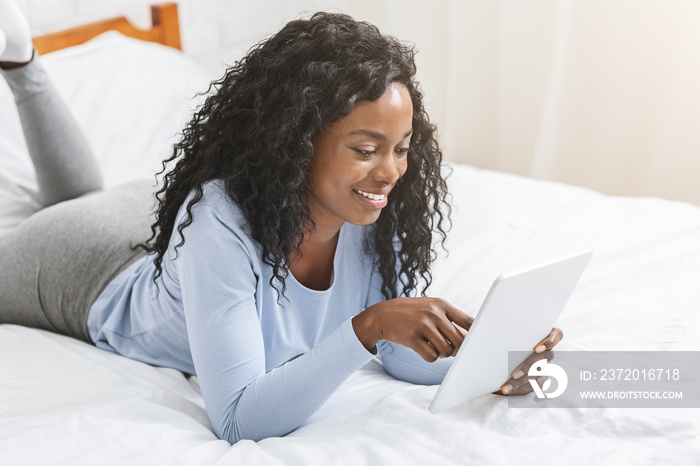 Girl reading blog on digital tablet in bed, touching screen