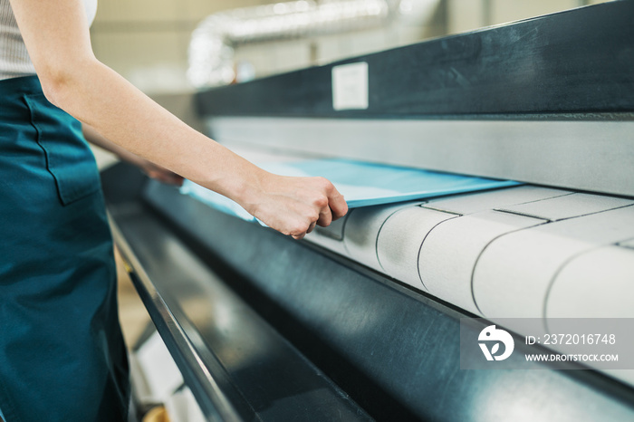 Young laundry worker pats the linen on the automatic machine at the dry cleaners.