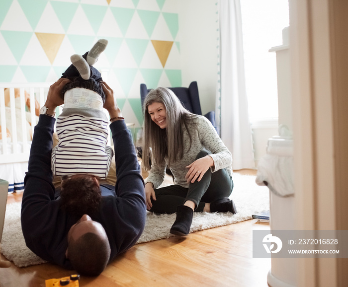 Happy mother sitting by playful father picking up son upside down while lying on rug at home