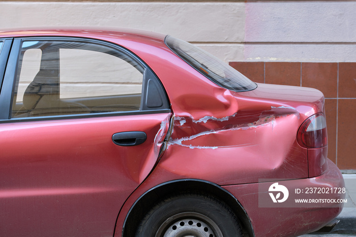 Dented car with damaged body parked on city street side. Road safety and vehicle insurance concept