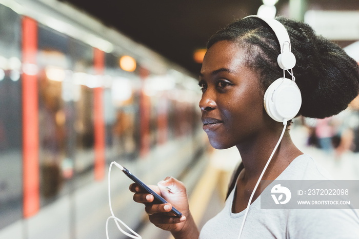 Half length of young beautiful afro black woman traveling on underground, listening music with headp