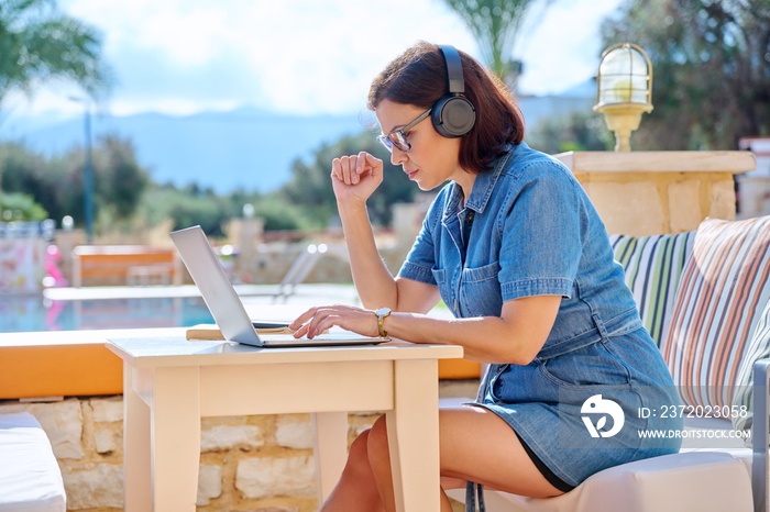 在户外工作的成熟女性，戴着耳机，使用笔记本电脑。