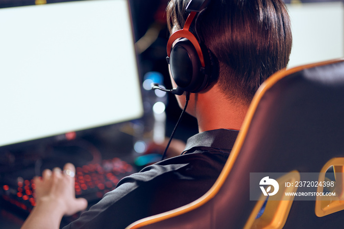 Rear view of a male cybersport gamer wearing headphones playing online video games while sitting in 