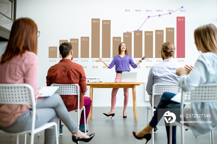 Young woman speaker reporting to the audience during the meeting in the conference room with charts 