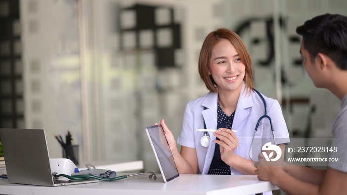 Asian female doctor using tablet computer and talking to male Asian patient