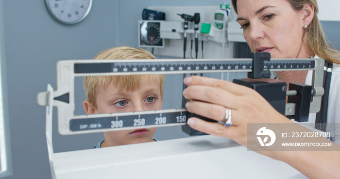 Doctor weighing little boy patient on scale in exam room. Female pediatrician and child performing r