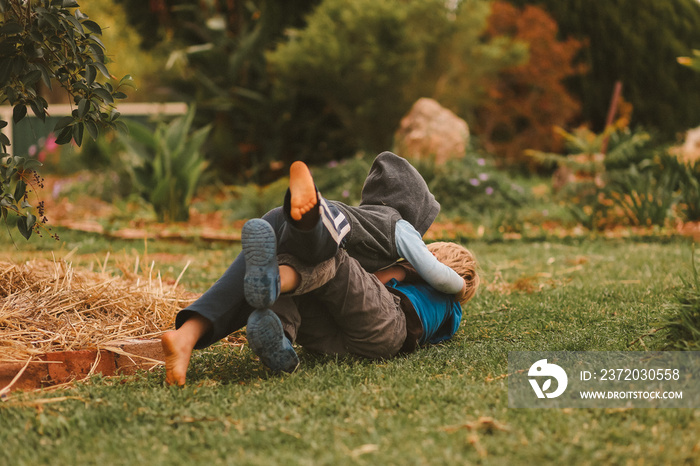 Little boys wrestling and play fighting on green lawn surrounded by gardens