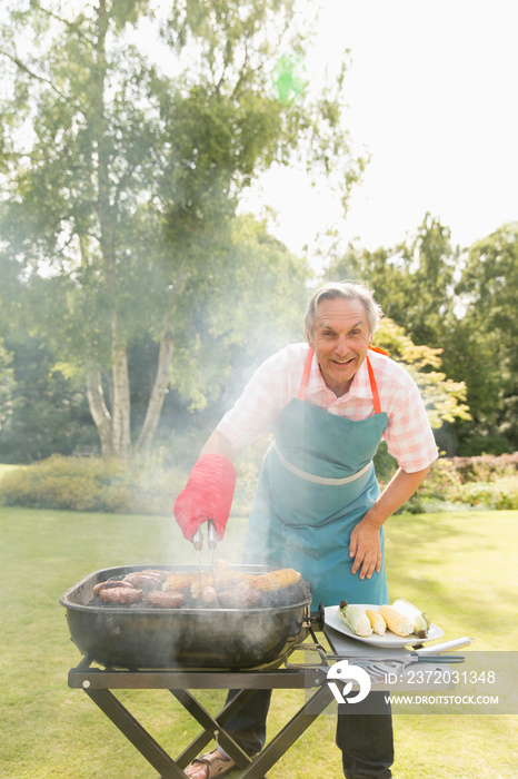 Portrait happy senior man barbecuing in sunny backyard