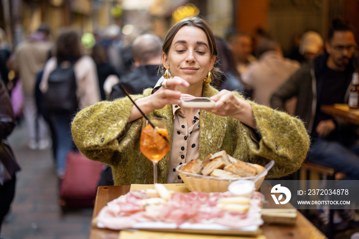 坐在餐厅里，一位女士拿着意大利肉类开胃菜和雪碧Aperol饮料拍照